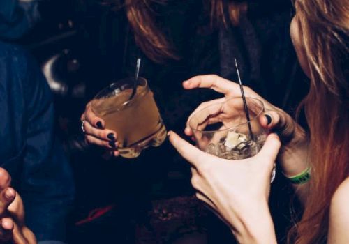 People are socializing, holding drinks, and smiling in a lively atmosphere.