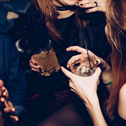 People are socializing, holding drinks, and smiling in a lively atmosphere.