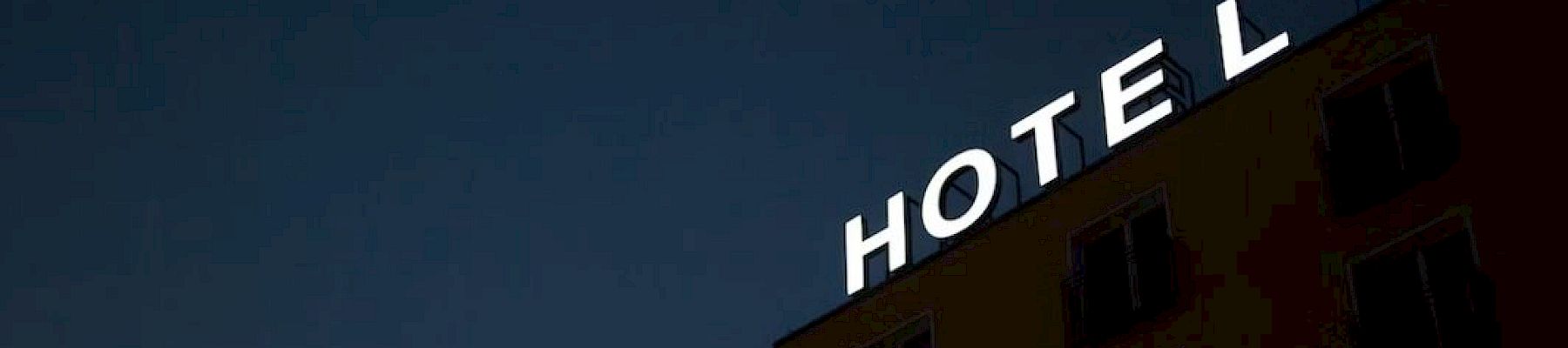 A building with a partially lit "HOTEL" sign against a dark sky, the "H" is missing some illumination.