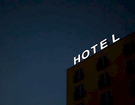 A building with a partially lit "HOTEL" sign against a dark sky, the "H" is missing some illumination.