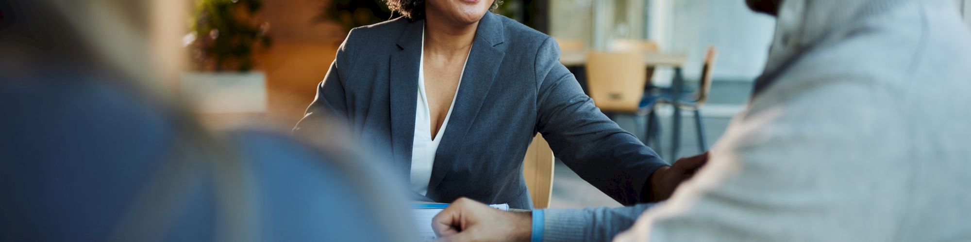 Three people are having a friendly conversation in an office setting, with a focus on a smiling woman.